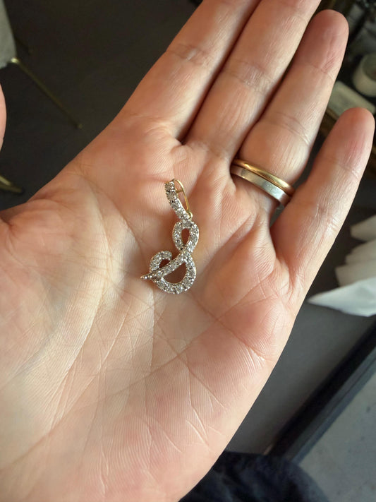Dije letra "&" XL cursiva en oro y diamantes.